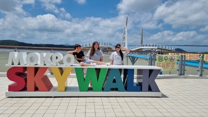 A group of youth in front of a sign that reads Mokpo Skywalk. Behind them, the skywalk.